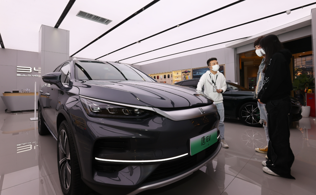 比亚迪店内，一名销售人员（左）正在向两位顾客介绍车辆信息